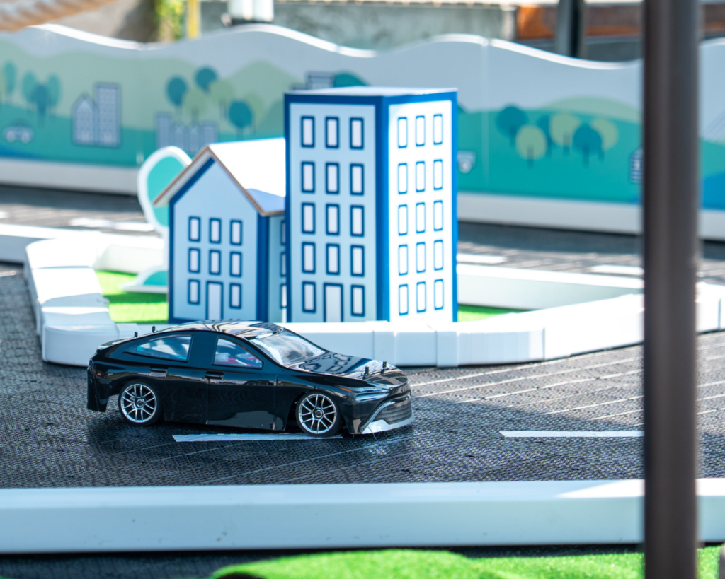 A hydrogen-powered RC car drives on a miniature city track with model buildings during the Hydrogen Pitstop event.