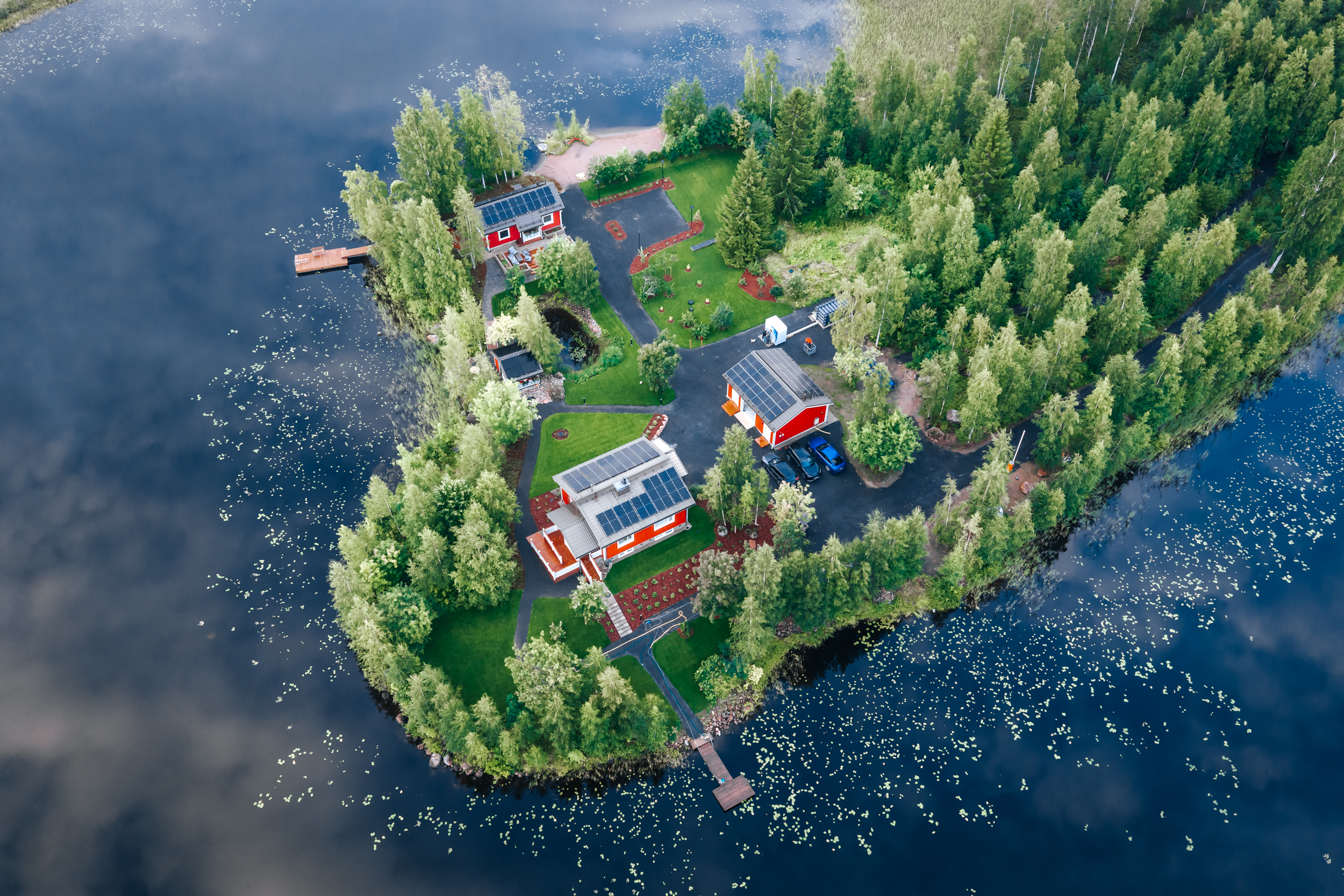 Aerial view of a wooded lakeside property with several red buildings, lawns, and docks.