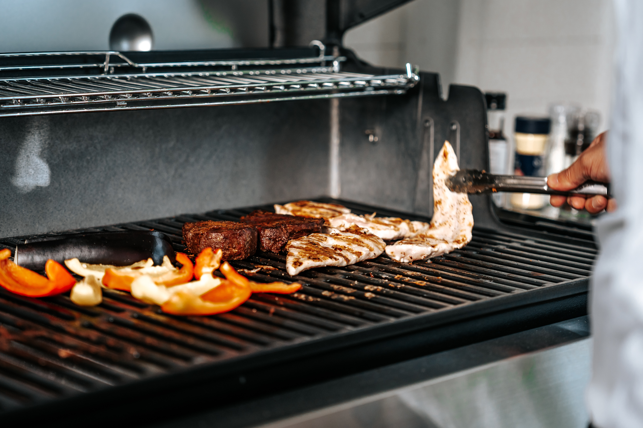 Meat and vegetables cooking over an open flame on a commercial-style grill.