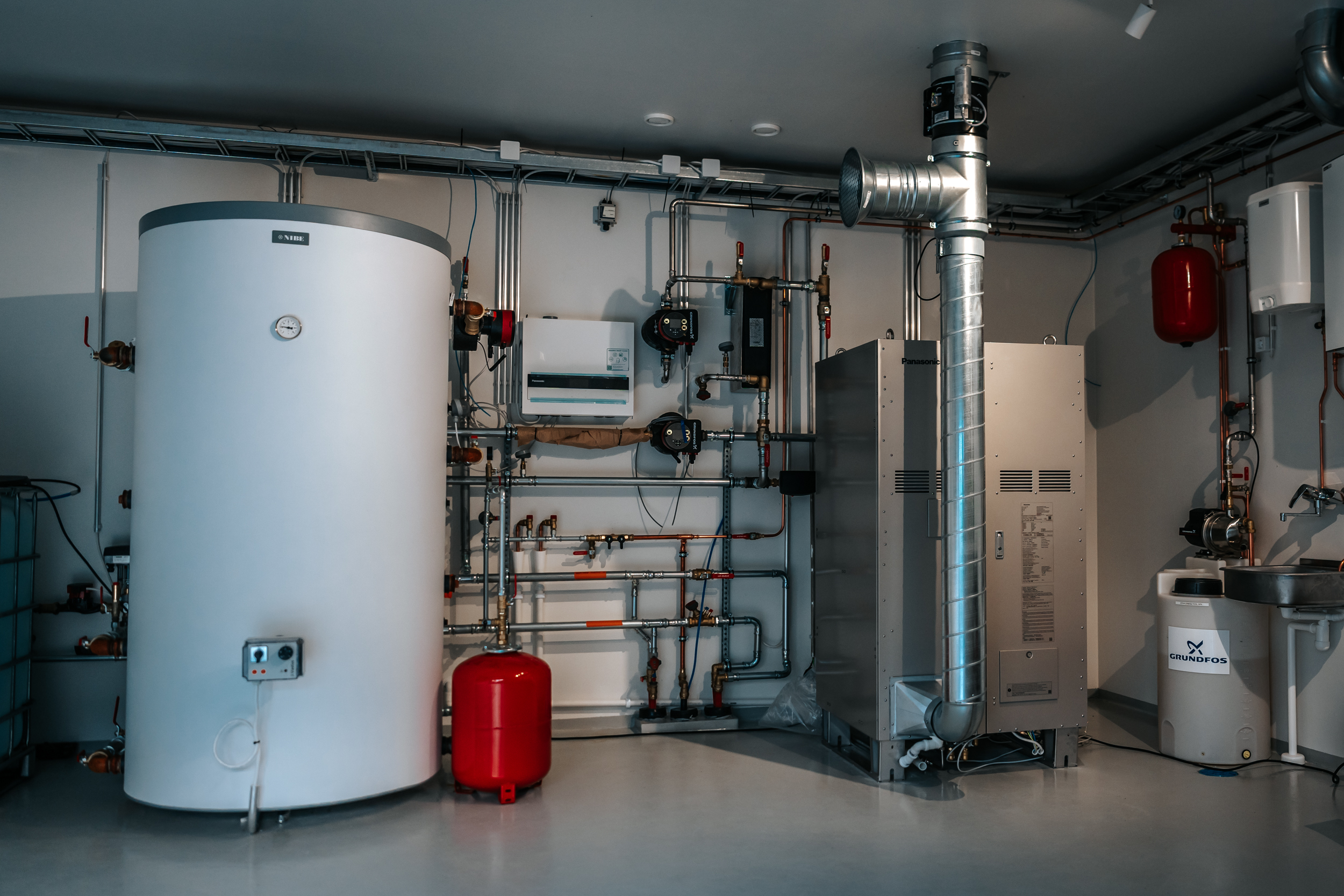 Technical room containing a large water tank, pipework, ventilation ducts, and heating equipment.