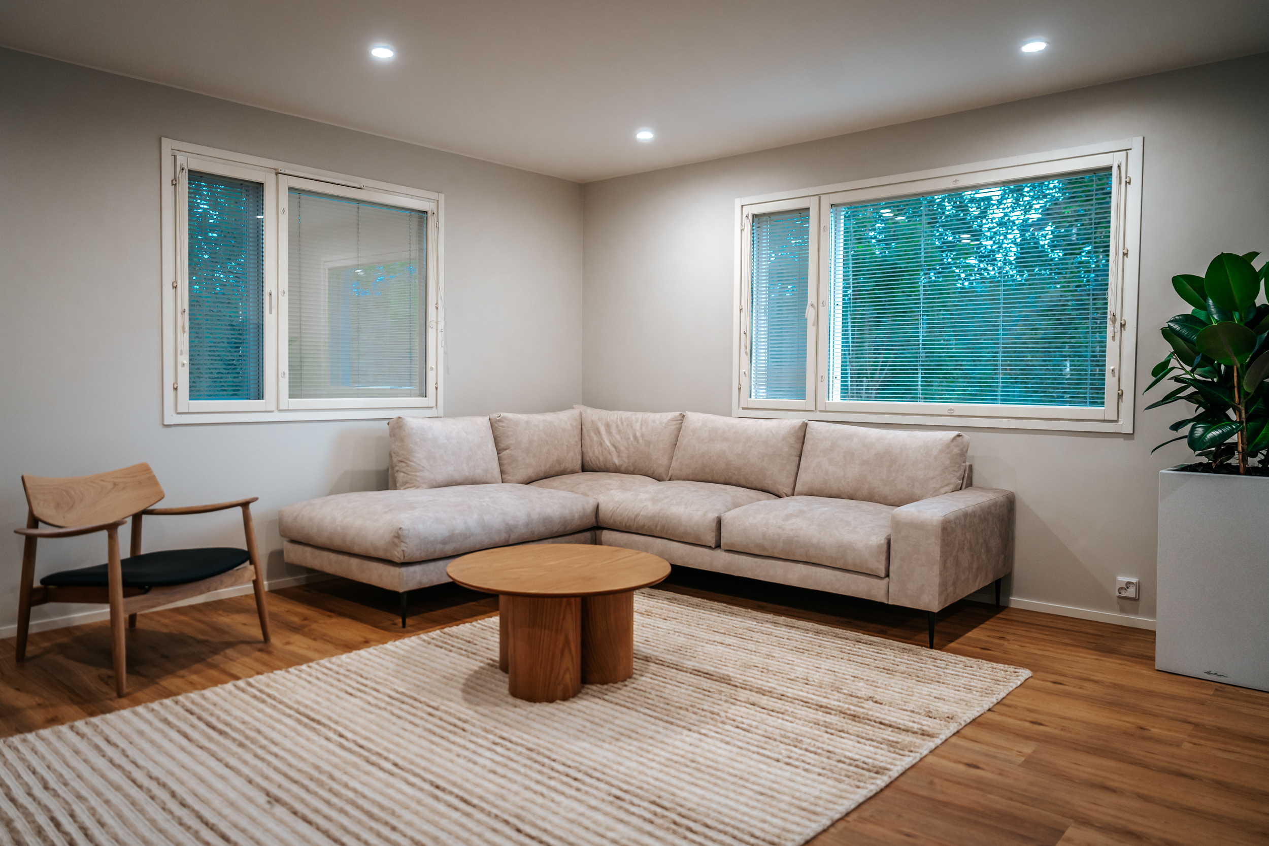 Bright living room with a beige corner sofa, wooden coffee table, and large windows.